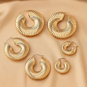 Three pairs of elegant gold pleated hoop earrings in different sizes on silk background