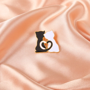 Enamel cat pin featuring black and white cats forming a heart on pink satin silk background
