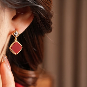 Close-up of geometric red and gold dangling earrings worn by a model in warm light