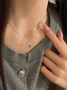 Close-up of S925 silver necklace with black heart pendant and white bow detail on model
