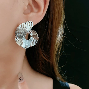 Macro detail of large silver spiral shell earrings worn by a model on dark background