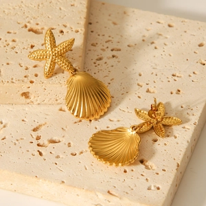 Golden stainless steel starfish and seashell drop earrings on a beige stone surface