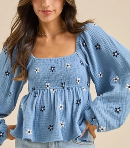 Détails de broderie florale blanche et bleu marine sur un haut bleu à col carré