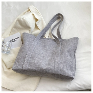 Detailed view of grey textured fabric tote bag on white surface with lifestyle props