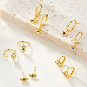 Golden evil eye hoop earrings set with blue and white zircon on white stone pedestal