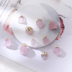 Natural pink crystal raw stone pendants with gold plated edges on marble tray