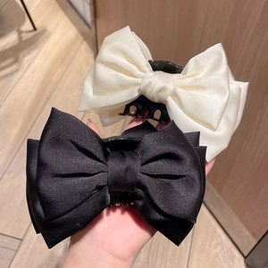Detail showing two satin bow hair clips in black and cream white with plastic claws