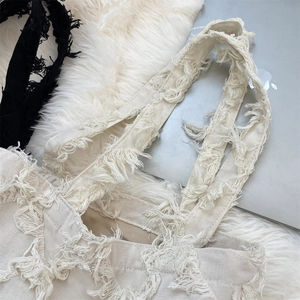 Flat lay detail of vintage canvas tote bag showing trendy frayed edges and tassel design