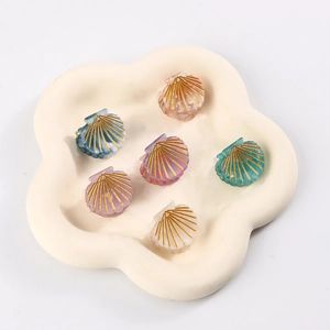Set kleiner Muschel-Haarklammern in Pastellfarben mit Goldakzenten auf Wolkentablett