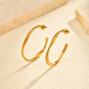 Chic twisted gold C-shaped hoop earrings with a matte satin finish on a stone background