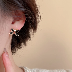 Gros plan d'une boucle d'oreille nœud en émail noir avec dorure portée à l'oreille