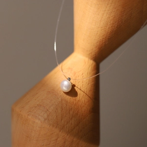 Detailed close-up of a 8mm white pearl pendant on a minimalist invisible fishing line necklace