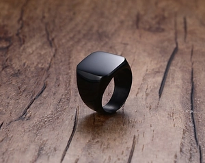 Detailed view of a black square signet ring for men on dark wood background surface
