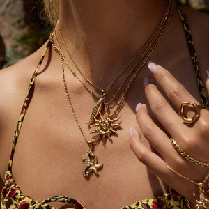 Close-up of layered gold stainless steel sun necklaces and geometric ring on a model