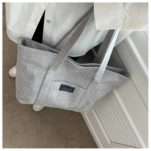 Detailed view of grey canvas tote bag featuring a stitched black FASHION label patch