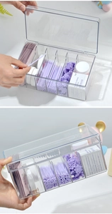 Detail of 6-compartment clear acrylic lash storage box with hinged lid on white desk