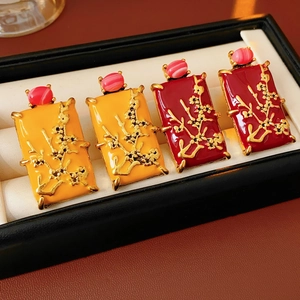 Détail de boucles d'oreilles carrées en émail vintage orange et rouge foncé avec motifs dorés