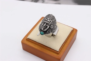 Dettaglio dell'anello dorato con maschera indiana, piume e pietra di turchese