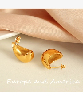 Detailed view of polished golden water drop earrings on soft pink silk fabric background