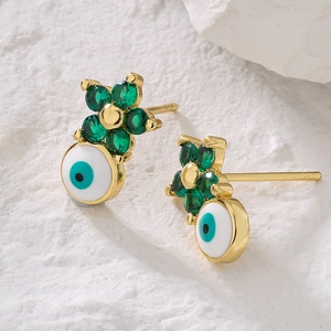 Gold evil eye stud earrings with green zircon flower detail on a white stone background