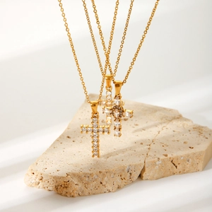 Gold cross pendant necklace with zircon stones on minimalist stone display