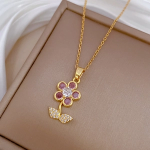 Macro detail of leaf and flower pendant with pink zircons on a gold chain necklace