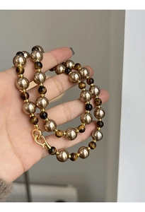 Détail des perles de bronze et pierres œil de tigre sur un collier perlé plaqué or