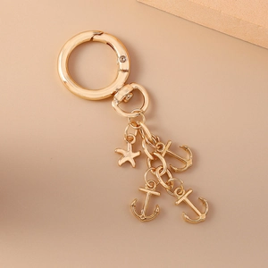 Golden alloy keychain featuring minimalist starfish and anchor charms on a beige background