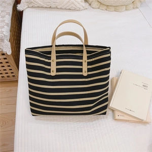 Close-up of a striped canvas tote with leather handles and gold studs on a bed