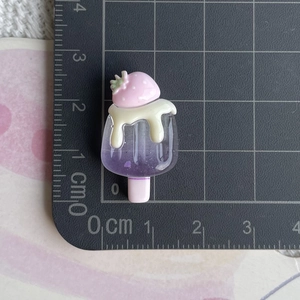 Vue macro d'une breloque popsicle fraise en résine de 3cm sur un tapis de coupe