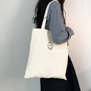 Large beige canvas tote bag featuring a minimalist black smiley face print on a side-worn model