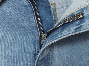 Dettaglio ravvicinato della cerniera in metallo e cuciture arancioni su denim azzurro