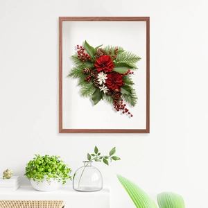 Christmas wall art with red flowers, pine cones, and berries in a light wood frame