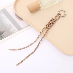 Close-up of golden rhinestone braided knot keychain on a beige display tray