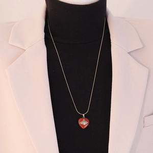 Close-up of a gold heart pendant necklace with eye detail on a model with a beige blazer