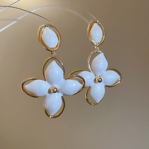 Détail de boucles d'oreilles fleur dorées avec résine blanche et tiges en acier