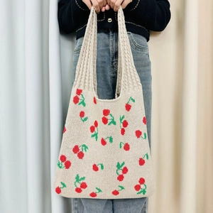 Detail of beige knitted tote bag featuring a red cherry pattern and woven texture