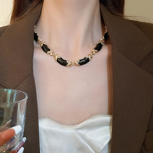 Gros plan d'un collier vintage en émail noir et maillons dorés en X sur un mannequin