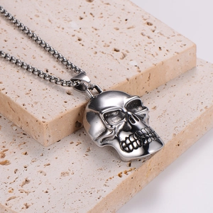 Polished stainless steel skull pendant necklace on a textured stone surface