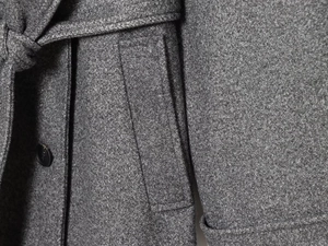Close-up of grey wool coat showing belt detail, textured fabric, and premium stitching