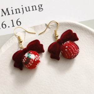 Detail view of festive red velvet bow earrings with red and green plaid fabric balls