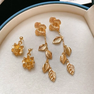 Detailed macro view of golden floral studs and long leaf fringe earrings in a gift box