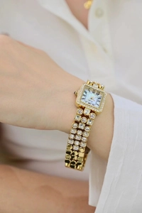 Detail of square gold watch with diamond-set bezel and mother-of-pearl dial on wrist