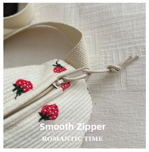 Detail showing the smooth zipper and strawberry embroidery on white corduroy fabric