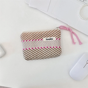 Close-up of a striped woven makeup pouch with pink accents on a clean white desk