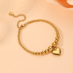 Gold stainless steel beaded heart bracelet with lobster clasp on warm orange background