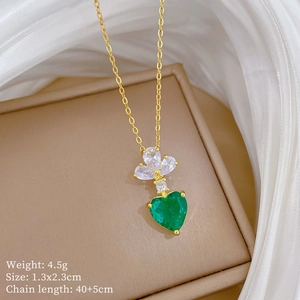Detail of luxury gold necklace with green heart gem and flower pendant on silk