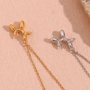 Detailed close-up of 18K gold and silver balloon dog pendants on light pink textured surface