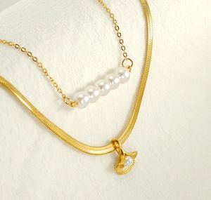Detail of layered gold ginkgo leaf and pearl pendants on elegant herringbone snake chains