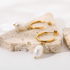 Close-up of golden hoop earrings with natural baroque pearl charms on a stone display